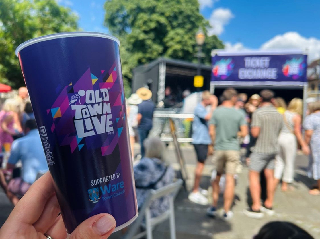 A branded reusable event cup held up in front of an outdoor live-event crowd